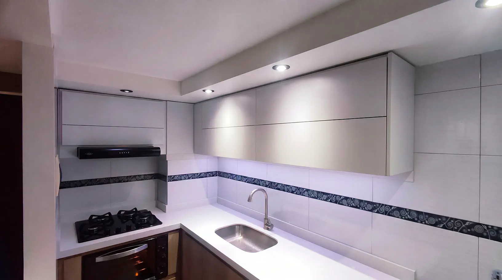 Cocina integral pequeña y moderna con gabinetes blancos, iluminación LED bajo mueble y acabados en madera oscura