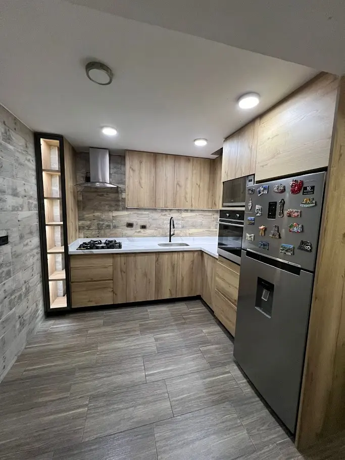 Cocina integral a medida combinando texturas de madera clara con salpicadero rústico gris y electrodomésticos empotrados