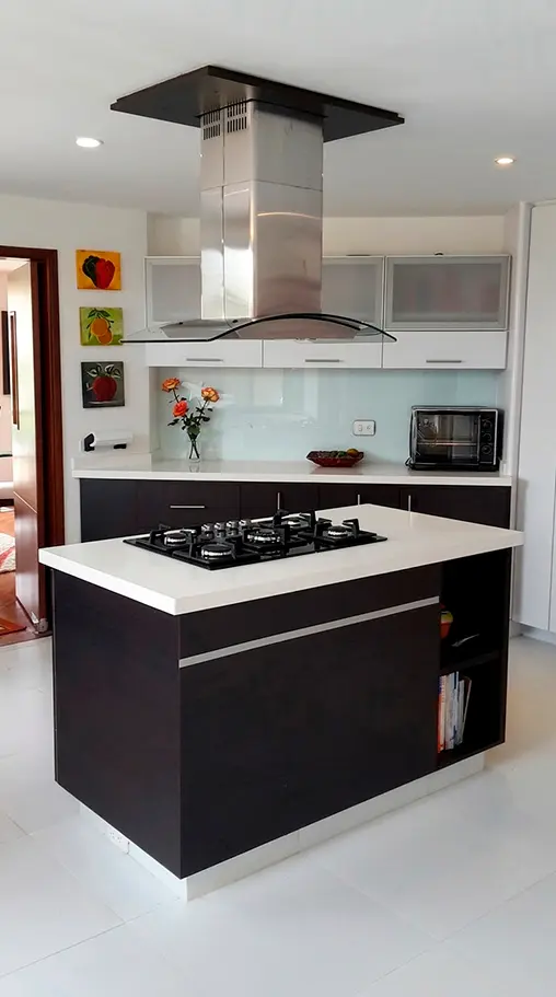 Diseño de cocina integral moderna con isla central, campana extractora en acero inoxidable y gabinetes oscuros en Bogotá