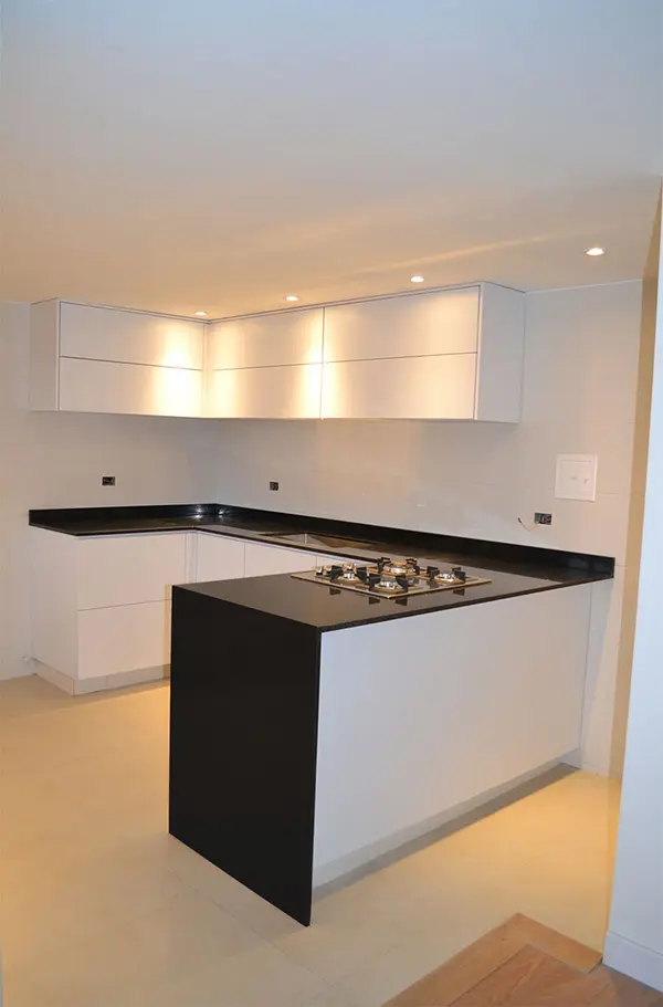 Cocina integral moderna a medida con gabinetes blancos iluminados y mesón en granito negro tipo península