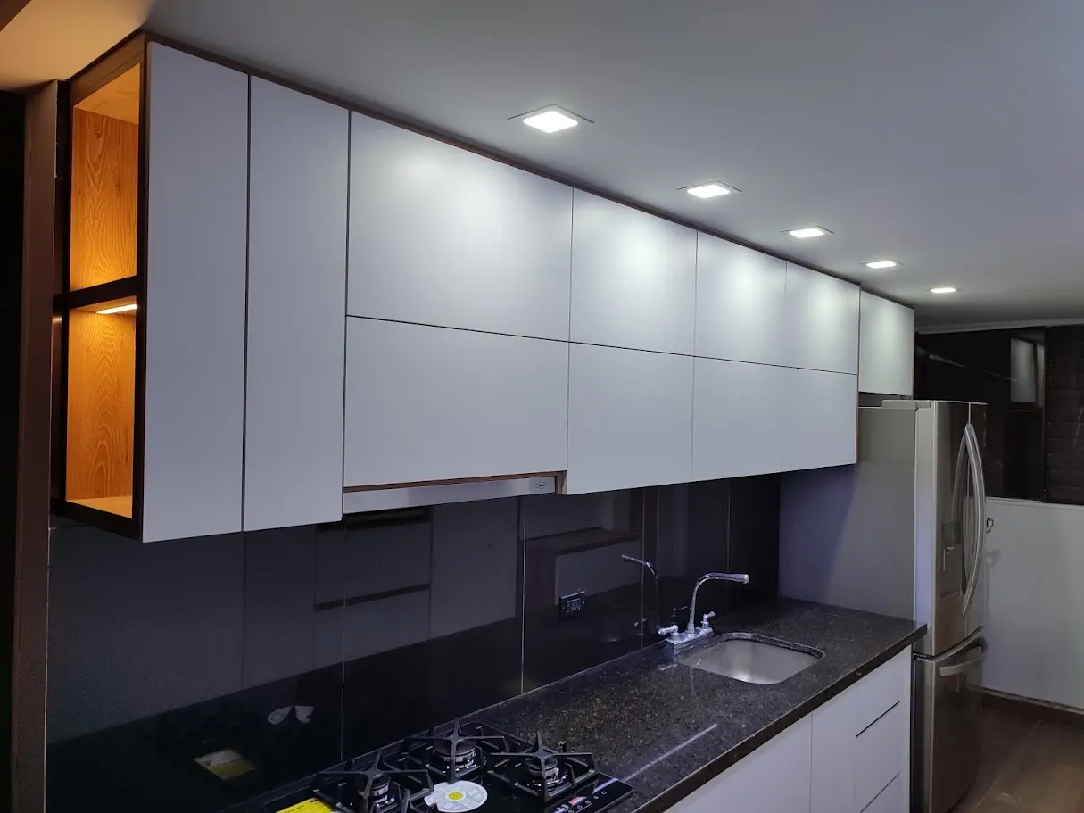 Detalle de cocina integral moderna con gabinetes blancos y repisa abierta en madera iluminada en Bogotá