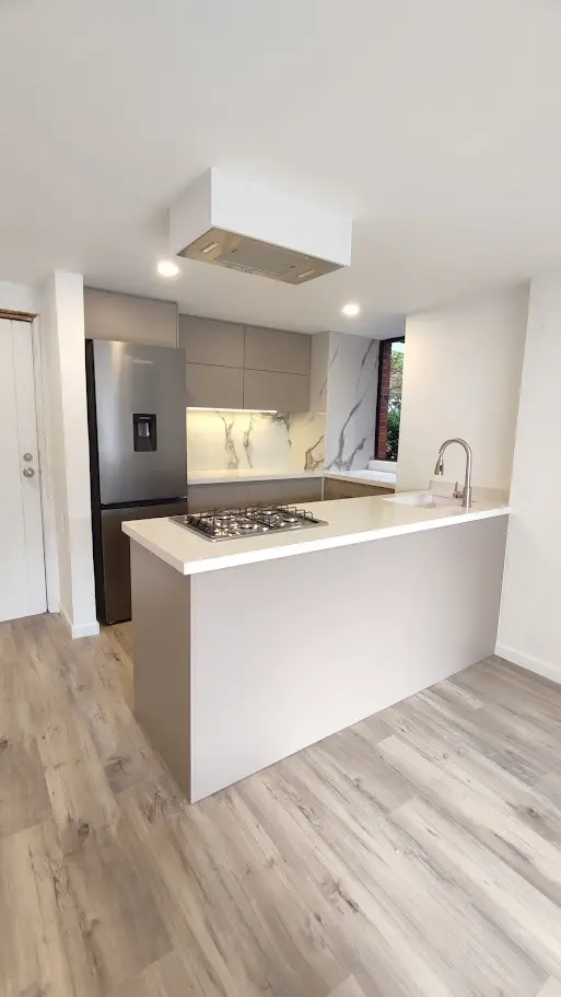 Cocina integral moderna con península, gabinetes color taupe mate y elegante salpicadero en formato mármol blanco