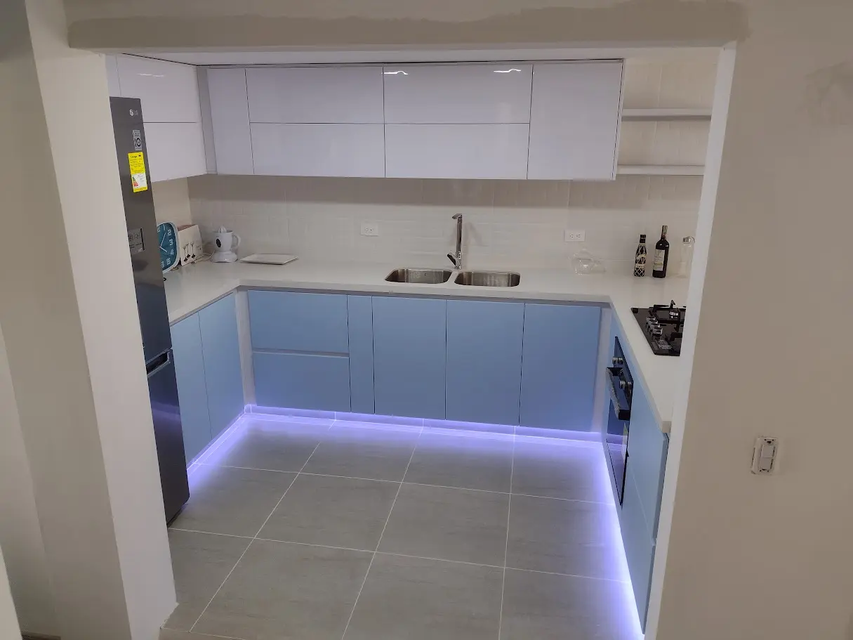 Cocina integral en forma de U con diseño moderno, muebles bajos azul pastel, altos en blanco e iluminación LED en el zócalo