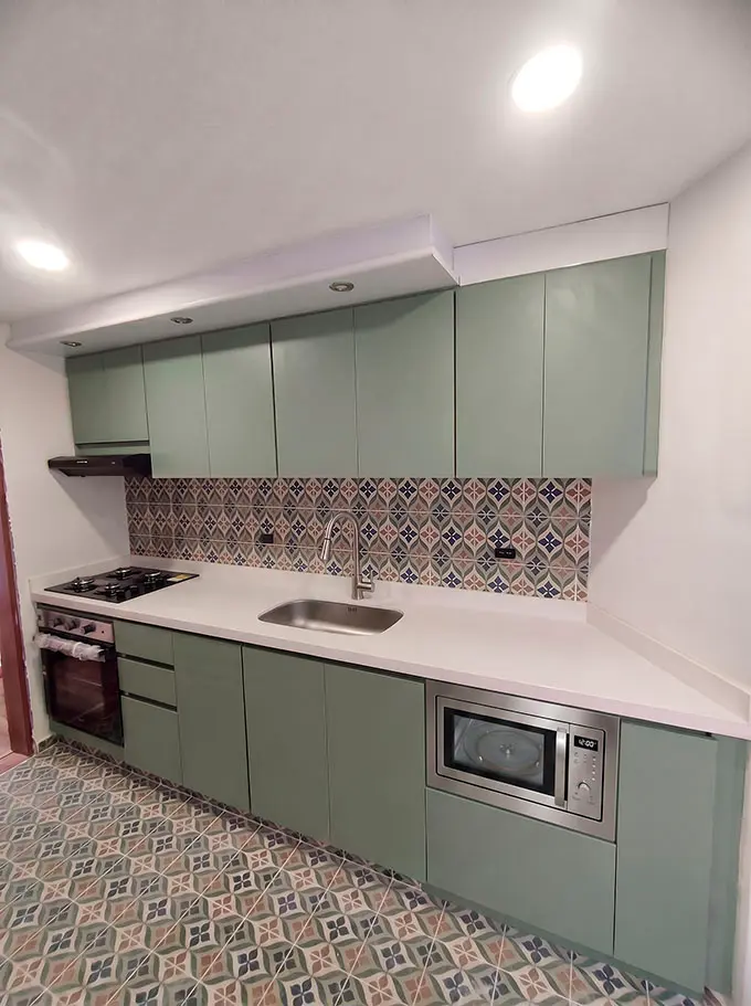 Hermosa cocina integral con gabinetes modernos color verde agave sin manijas, salpicadero decorativo y mesón blanco