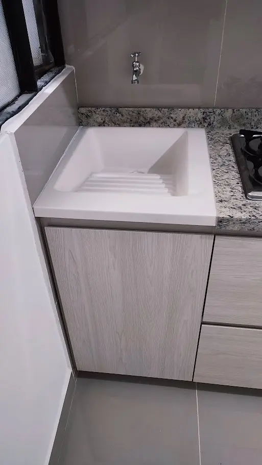 Detalle de lavaplatos moderno blanco integrado en un mesón de granito claro para cocina integral a medida