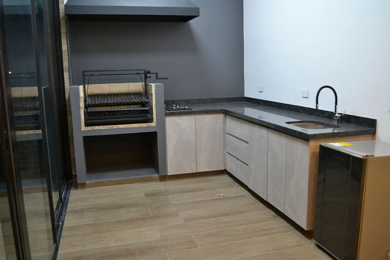 Diseño de zona BBQ con asador de ladrillo, gabinetes en madera clara y mesón de granito oscuro en Bogotá